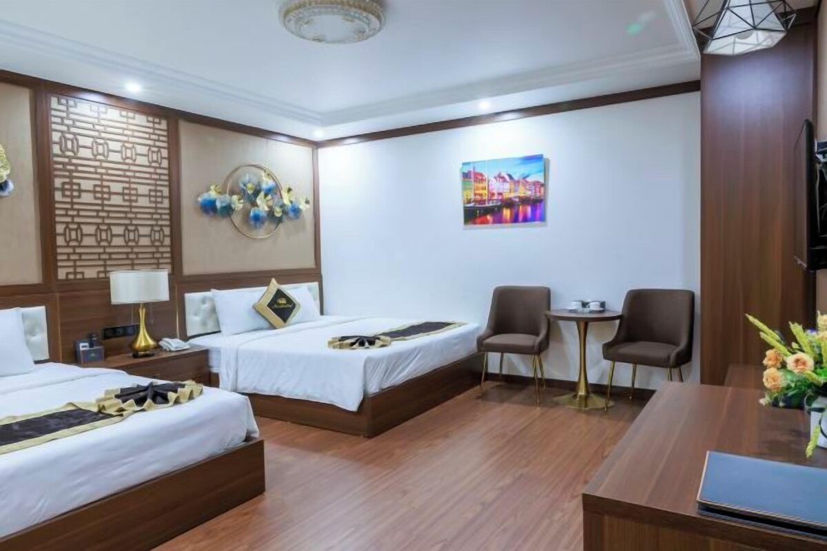 A hotel room with two beds, a desk, a chair, a small table, a decorative wall panel, and a painting.
