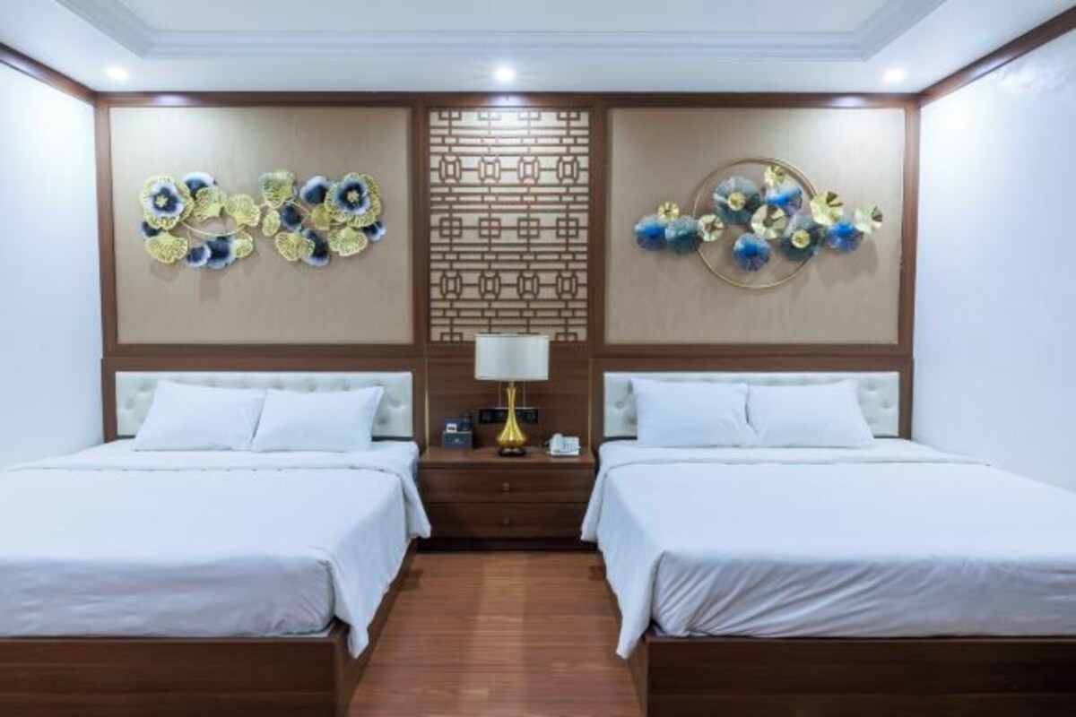 Habitación de hotel con dos camas, cabecero de madera, panel decorativo en la pared y mesita de noche con lámpara.
