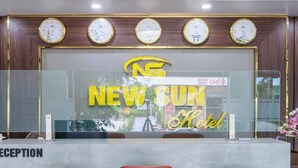 Zona de recepción con suelo de mármol, tres taburetes rojos, un mostrador de recepción y una pared con relojes y un letrero que dice "NEW SUN Hotel".