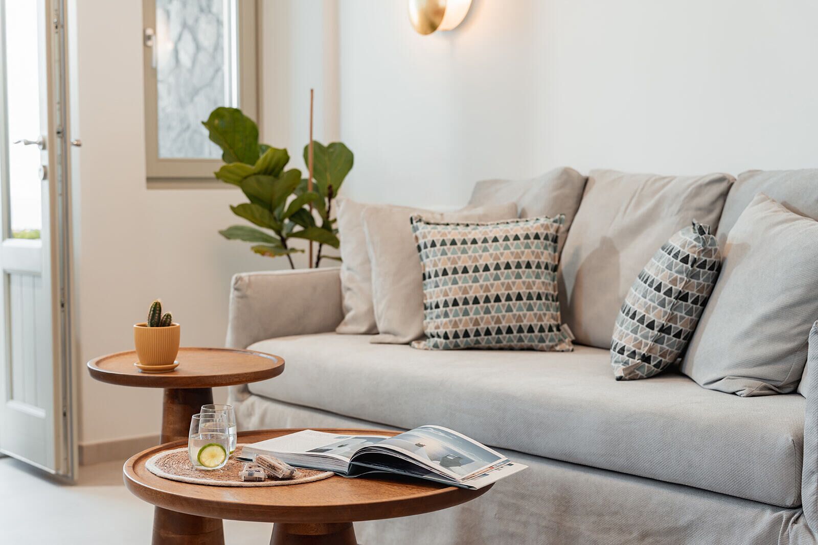 Ein gemütliches Wohnzimmer mit einer Couch, einem kleinen Holztisch, einem Glas Wasser, einer Zeitschrift und einer Topfpflanze.