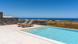 Una piscina con sillones de descanso y un muro de piedra, con vistas a un paisaje costero.