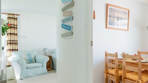 A room with a light blue sofa, a wooden dining table with chairs, and a wall with directional signs. - Wonderful private villa for 4 guests with WIFI, TV and patio (Bodmin)