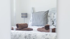 A neatly made bed with a floral-patterned bedspread and two rolled-up towels.