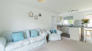 A modern living room with a light blue sofa, a matching armchair, and a kitchen area with a dining table and bar.