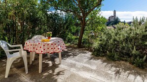 An outdoor dining area with a table and chairs, surrounded by greenery and a view of a historic building with a tower.