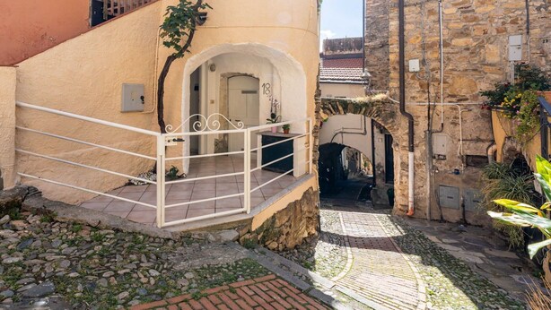 A narrow alleyway with a stone building on the right and a beige building on the left.