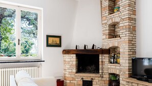 A cozy living room with a brick fireplace, a comfortable sofa, wicker ottomans, and a television.