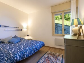 A bedroom with a bed, bedside lamps, a window with a view of greenery, and a lamp on a dresser.