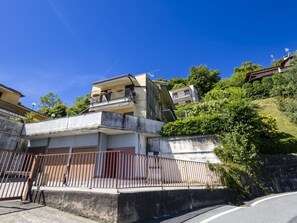 A multi-story residential building with balconies, a gated entrance, and a hillside backdrop.