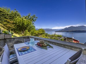 An outdoor dining area with a table set for two, overlooking a lake and mountains.