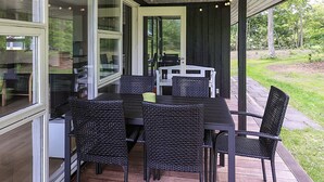 Un patio exterior con una mesa y sillas, rodeado por puertas y ventanas de vidrio, con vistas a un área verde.