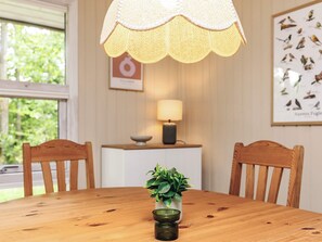 A wooden dining table with chairs, a hanging lamp, a framed bird illustration, and a small plant on the table. - 5 Person Holiday Home in Logstor (Logstor)