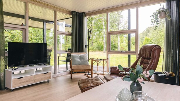 Un salón amplio con un televisor grande, asientos cómodos y ventanas grandes con vistas al exterior.