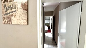 Ein Flur, der zu einem Schlafzimmer mit Bett, kleinem Tisch und Stuhl führt. An der Wand ist ein Holzschild mit dem Wort 'Beach' zu sehen.