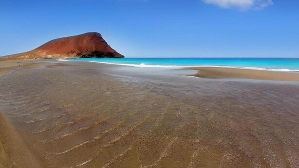 Une plage avec une grande formation rocheuse et une eau d’un bleu cristallin.