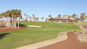 Un parcours de golf doté d’un club-house, de palmiers et offrant une vue sur un ciel dégagé.