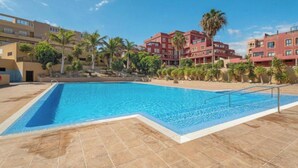 Une piscine entourée de palmiers et d’immeubles dotés de balcons.