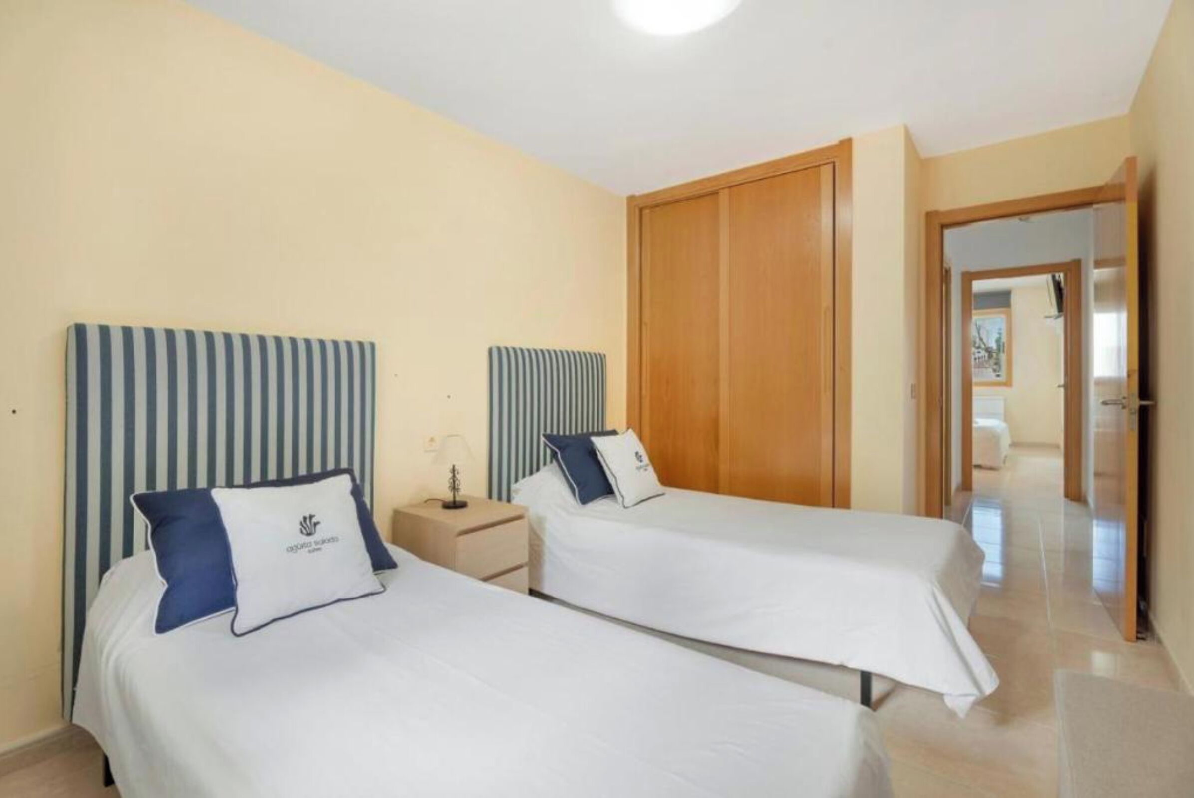 A hotel room with two single beds, a wooden wardrobe, a nightstand, and a mirror.