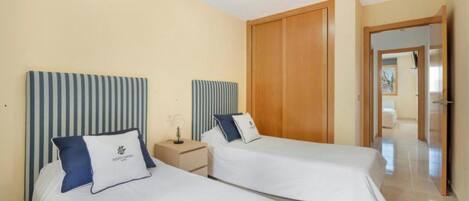 A hotel room with two single beds, a wooden wardrobe, a nightstand, and a mirror.