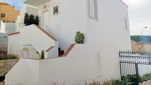 Ein weißes Gebäude mit roten Ziegeln auf dem Dach, einer Treppe und einem kleinen Garten.