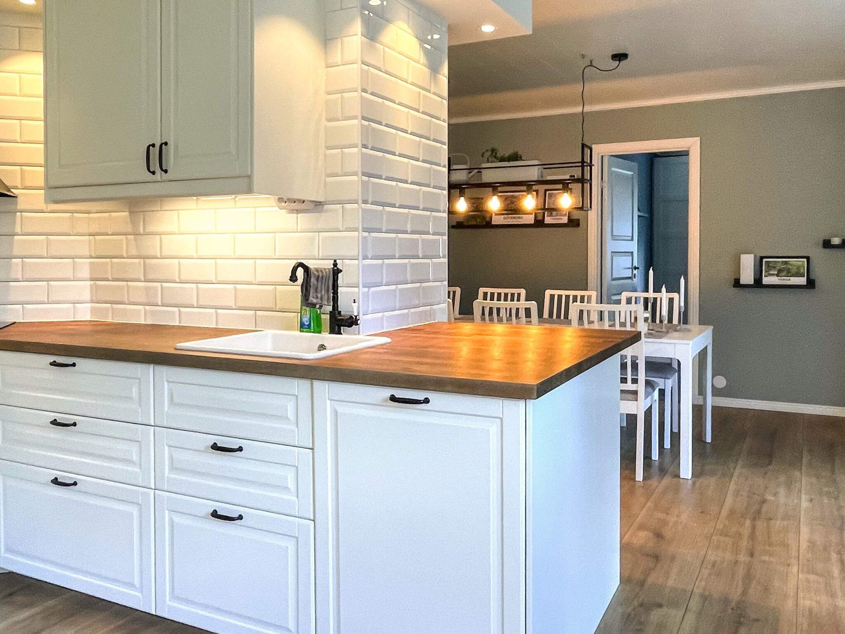 A kitchen with white cabinetry, a wooden countertop, and a dining area with white chairs.