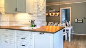 A kitchen with white cabinetry, a wooden countertop, and a dining area with white chairs.