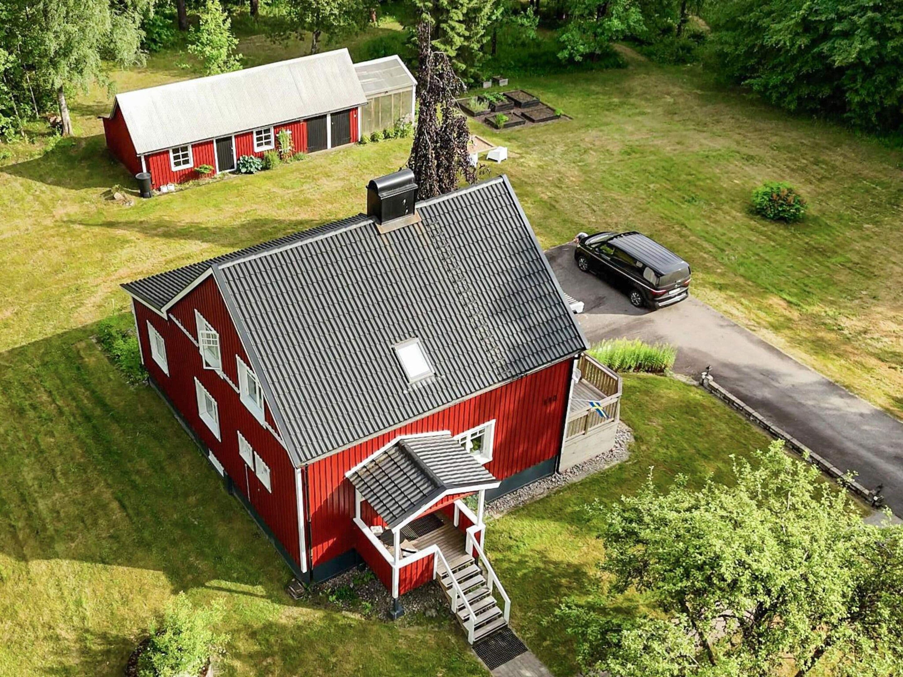 A red barn with a sloped roof, a covered porch, and a driveway leading to a parked car.
