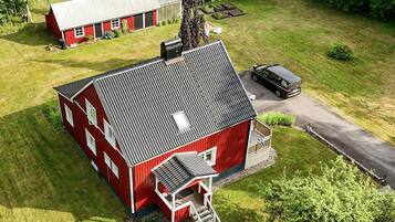 A red barn with a sloped roof, a covered porch, and a driveway leading to a parked car.