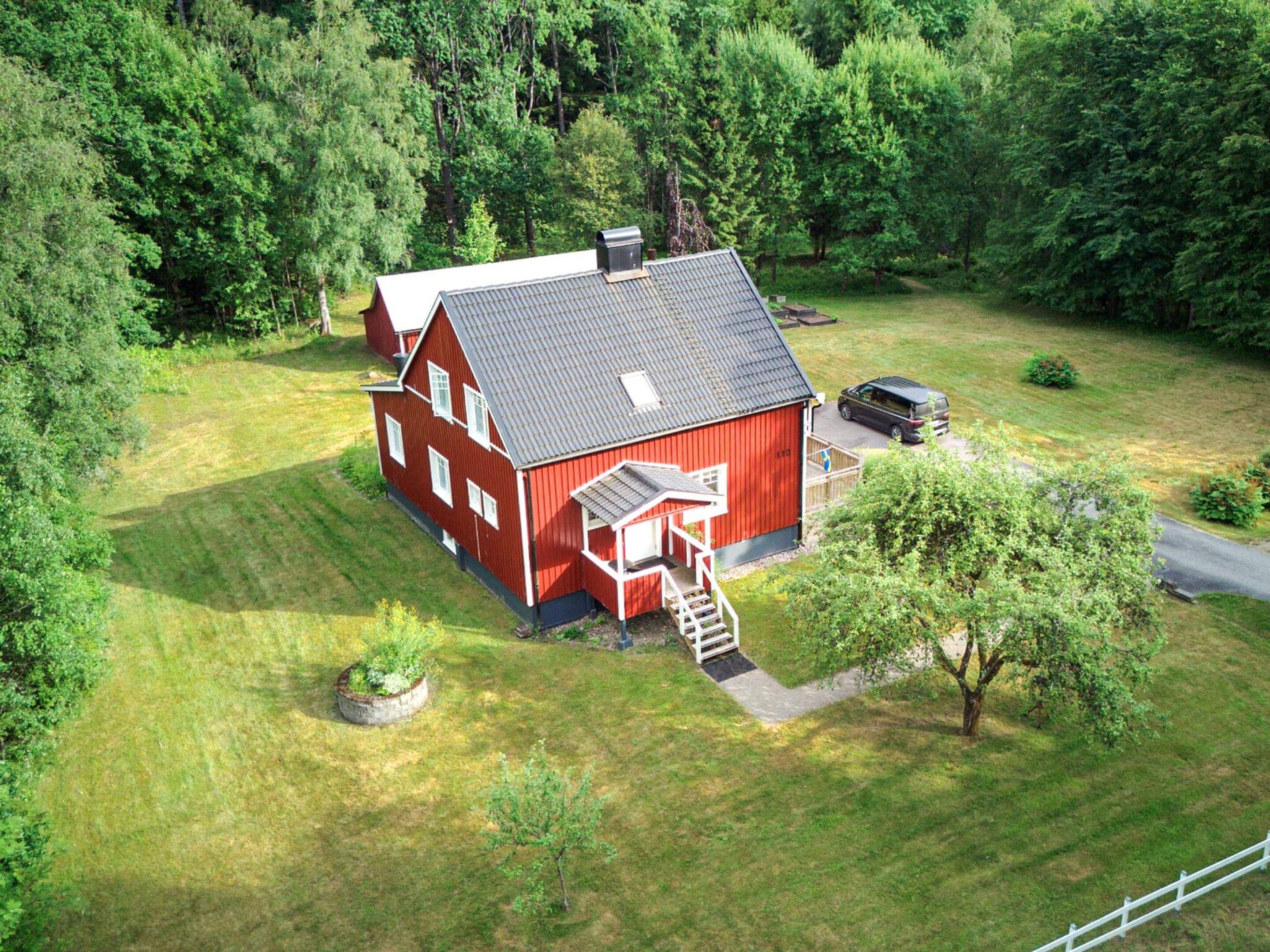 A red barn with a sloped roof, a covered porch, and a driveway leading to a parked vehicle.