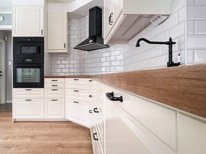A kitchen with white cabinetry, a black range hood, and a wooden countertop. - 4 Star Holiday Home in Tvarred (Tvärred)