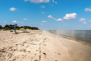 Ein Strand mit blauem Himmel, sandigem Ufer und einigen Sonnenschirmen.