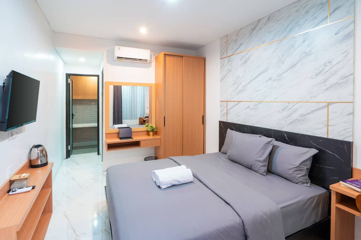 Quarto de hotel moderno com uma cama grande, televisão, escrivaninha e banheiro.