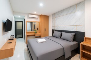 Una habitación de hotel moderna con una cama grande, un escritorio con espejo, una televisión y un equipo de aire acondicionado.