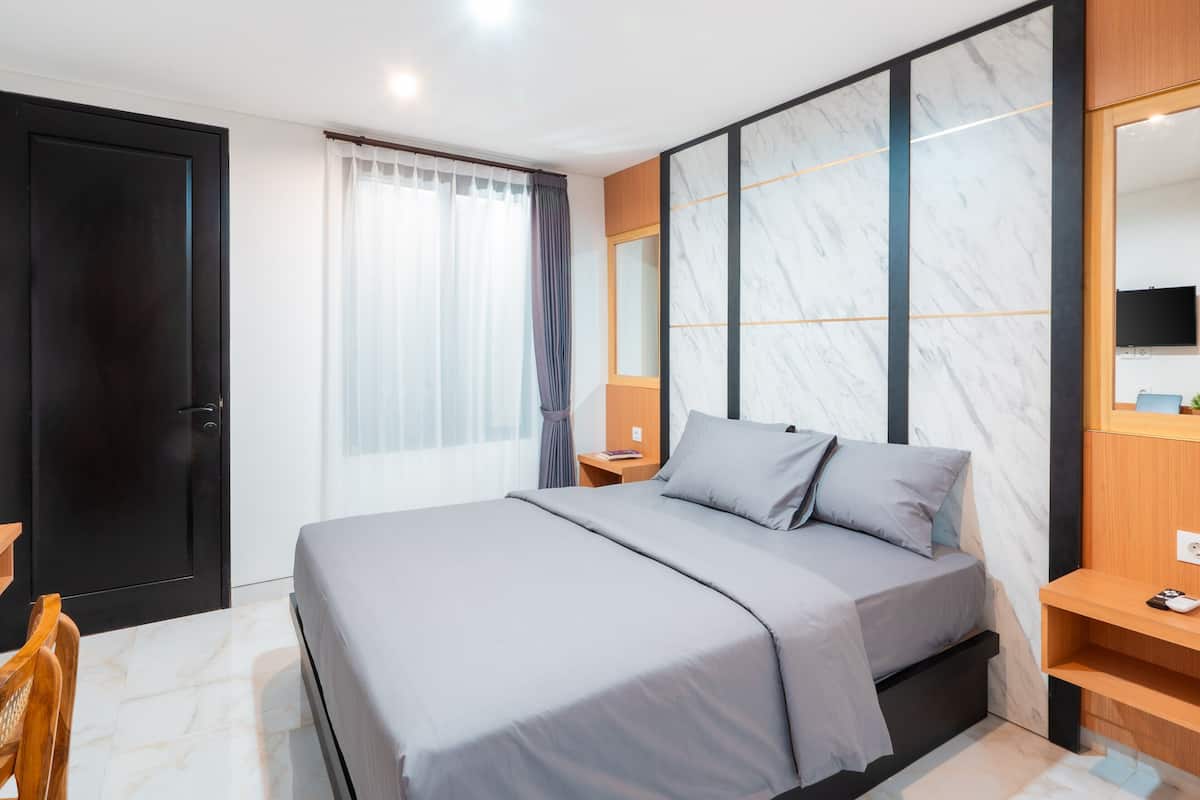 Quarto de hotel moderno com uma cama grande, uma mesa de cabeceira de madeira, uma escrivaninha com cadeira e um espelho grande.
