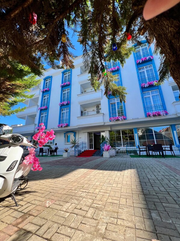 Un hôtel à la façade blanche, aux fenêtres bleues et aux balcons ornés de fleurs roses.