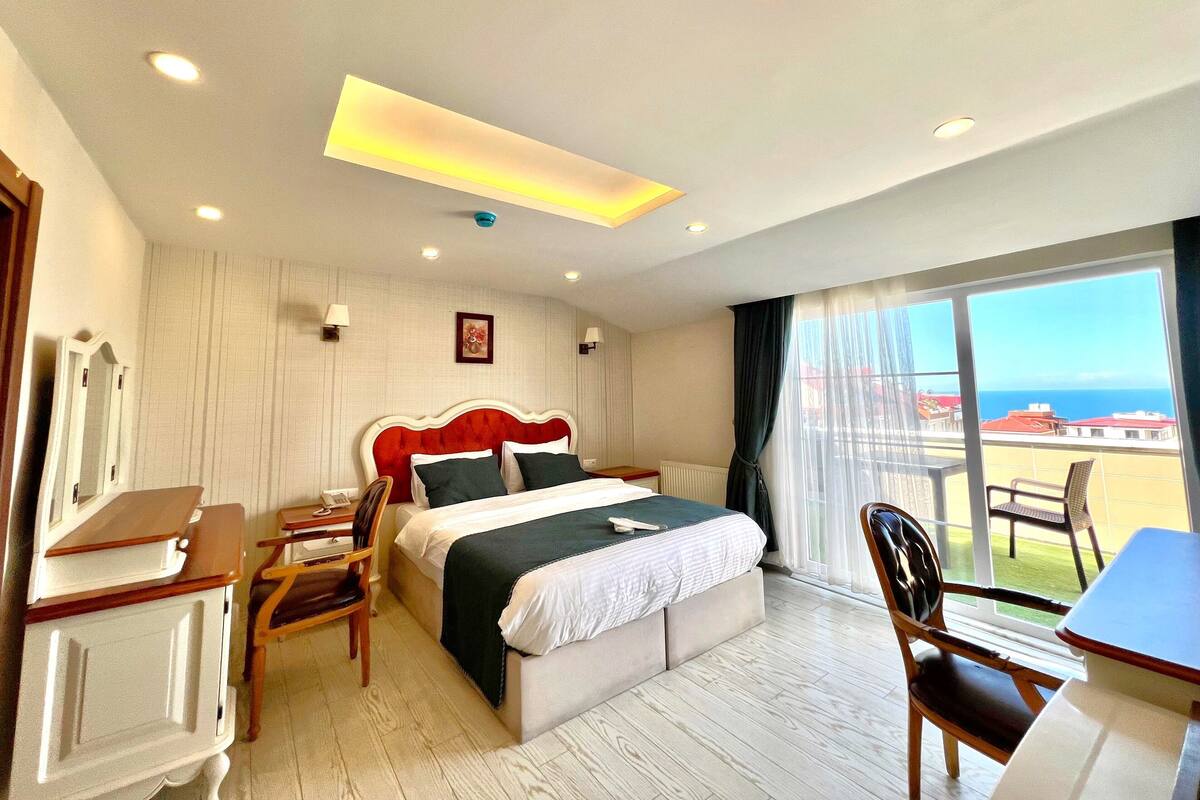 A hotel room with a bed, a desk, a chair, and a view of the sea.
