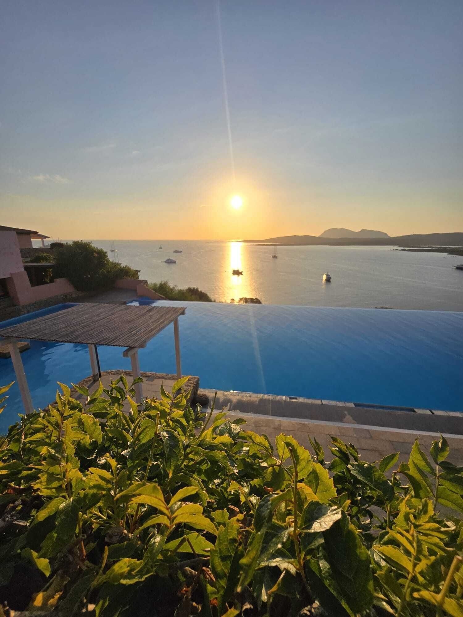 An infinity pool with a view of the sea and boats during sunset.