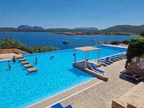 A swimming pool with clear blue water, a wooden deck, and lounge chairs.