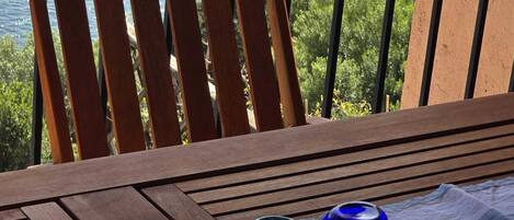 A wooden chair and a table with a tray of decorative glassware on a balcony overlooking a body of water.
