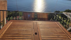 Une terrasse en bois offrant une vue sur une mer calme et des montagnes lointaines, sous un ciel dégagé.