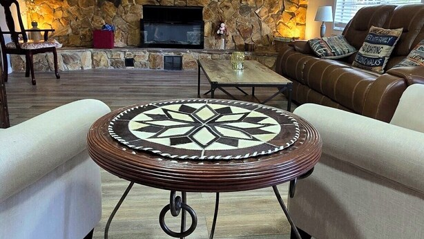 A living room with a stone wall, a ceiling fan, a fireplace, a TV, and a brown leather couch. - 3-bedroom with Lakeview, Free Kayaks and Game Room, Pets Allowed, Lanai & Grill (Inverness)