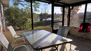 A covered outdoor seating area with a table and chairs, overlooking a body of water and greenery. - 3-bedroom with Lakeview, Free Kayaks and Game Room, Pets Allowed, Lanai & Grill (Inverness)