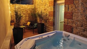 Eine gemütliche Außenpatio mit Whirlpool, Holzboden, Steinwänden und Lichterketten.