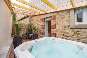 A spa area with a hot tub, wooden deck, stone walls, and a covered seating area. - Charming Duplex with Jacuzzi, Guingamp Center (Guingamp)