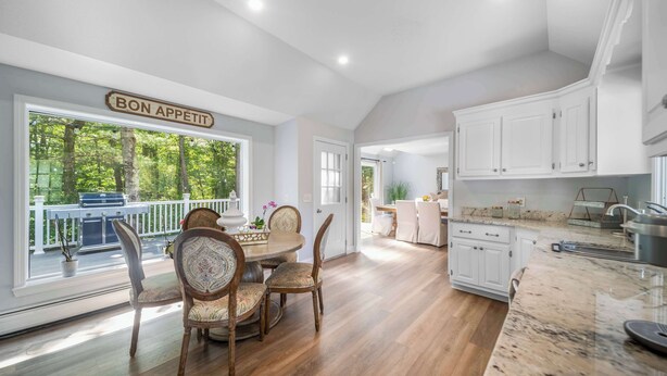 A spacious kitchen with white cabinets, a wooden dining table with chairs, and a large window overlooking a deck.