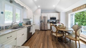 A modern kitchen with white cabinets, stainless steel appliances, and a dining area with wooden chairs.