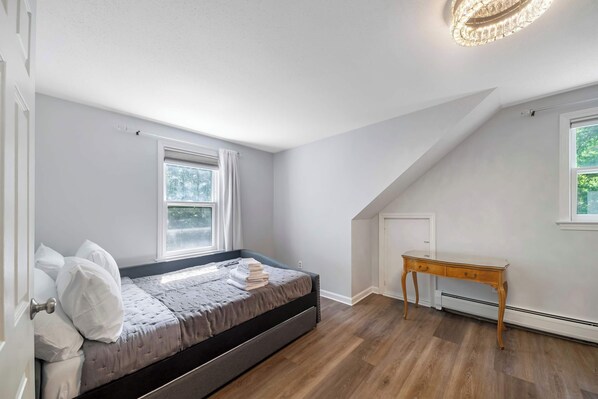 Un dormitorio con una cama, una mesita de noche de madera y un ventanal.