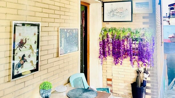 Comedor con pared de ladrillo, obras de arte enmarcadas, plantas colgantes y una mesa con sillas.