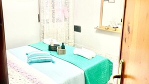 Un dormitorio con cama, mesita de noche, espejo y cortina.