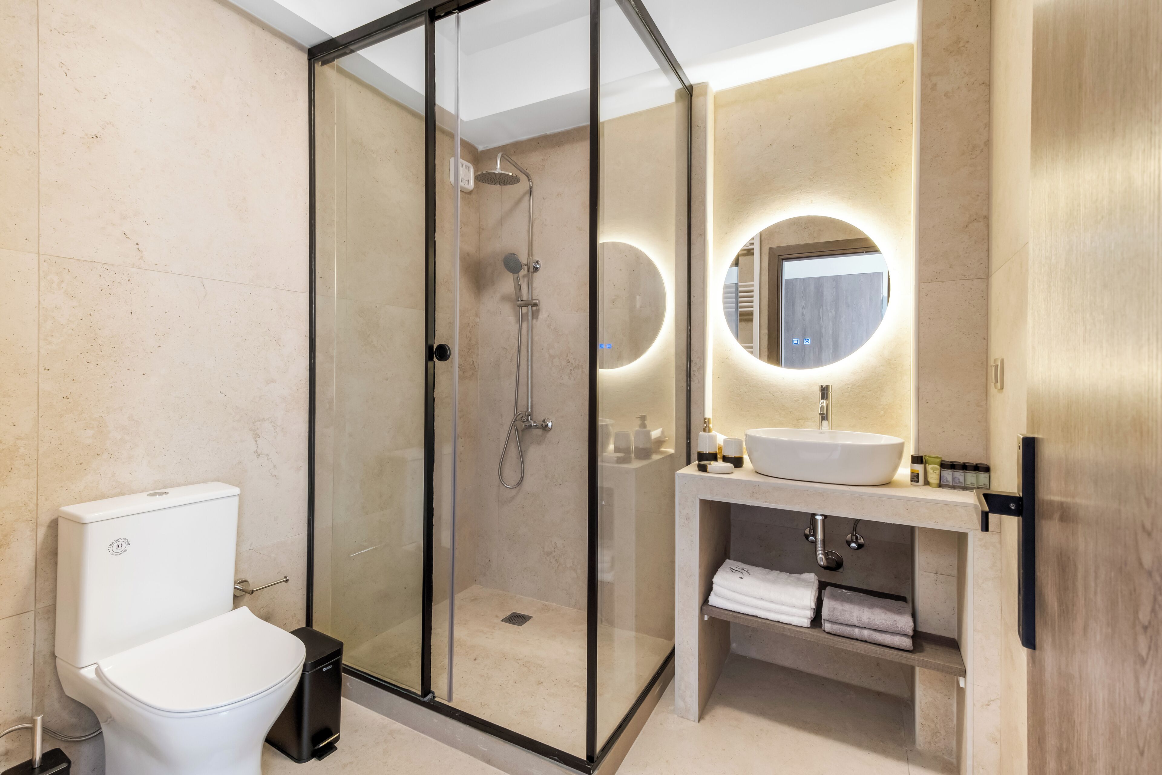 Een moderne badkamer met een douchecabine van glas, een wit toilet en een wastafel met een ronde spiegel en een inbouw wasbak.